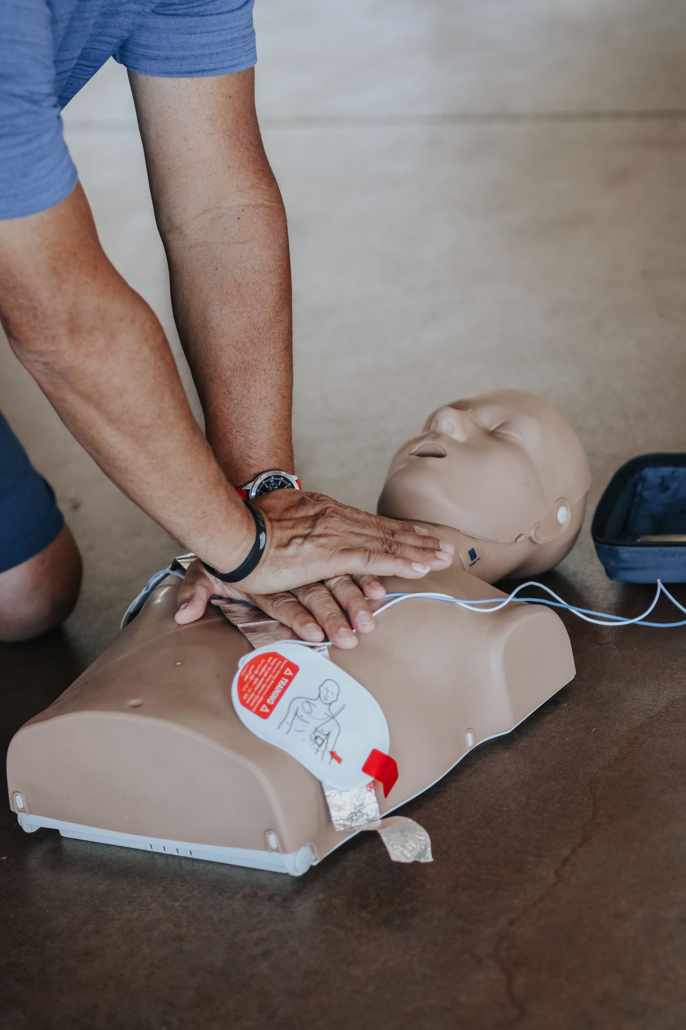 Hands performing CPR compressions on a training mannequin with AED pads