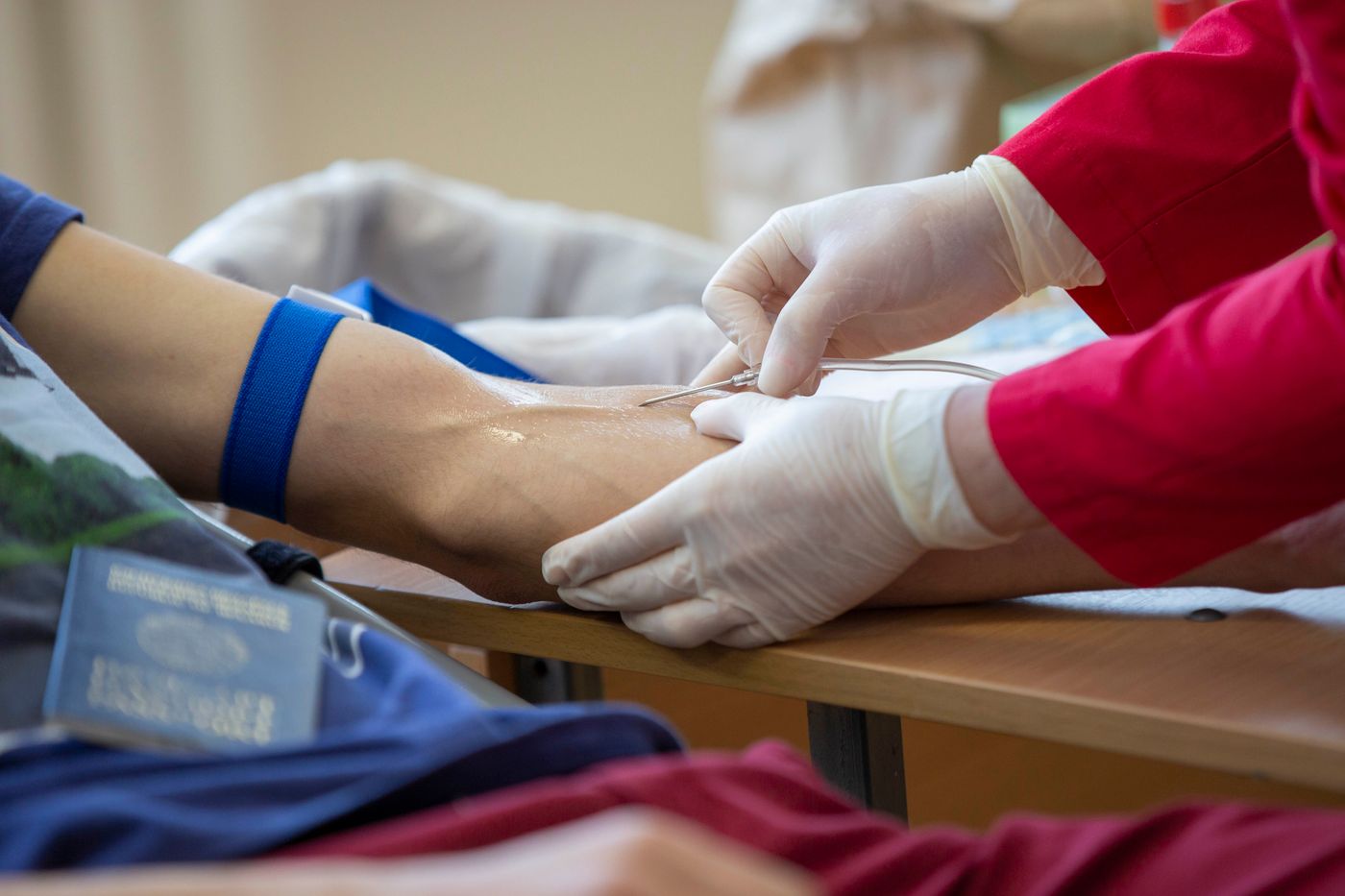 Gloved hands inserting an IV catheter into a patient's forearm with a tourniquet applied