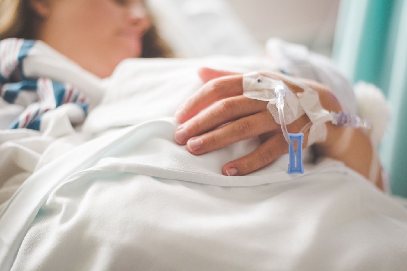 Peripheral IV catheter secured with tape and a transparent dressing on a patient's hand in a hospital bed