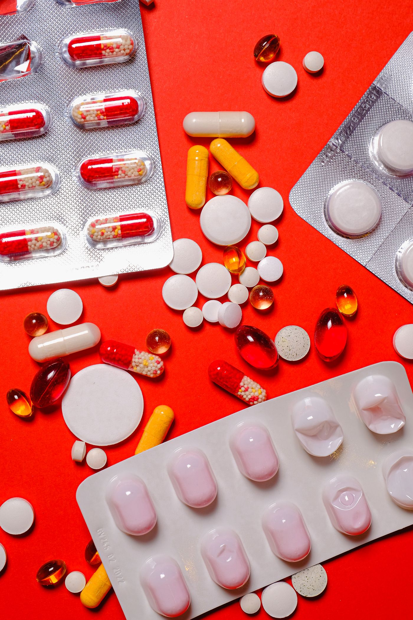 Assorted medication tablets and capsules in blister packs on a red surface