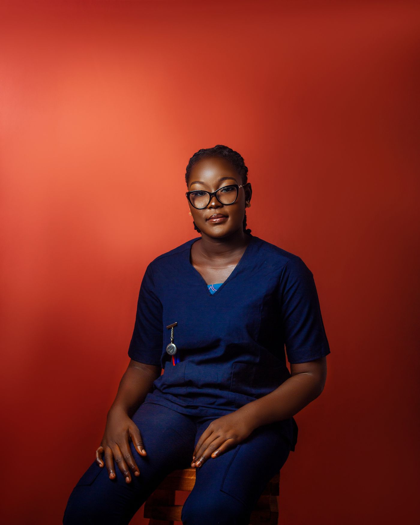 Confident new nurse in navy scrubs seated against a red background