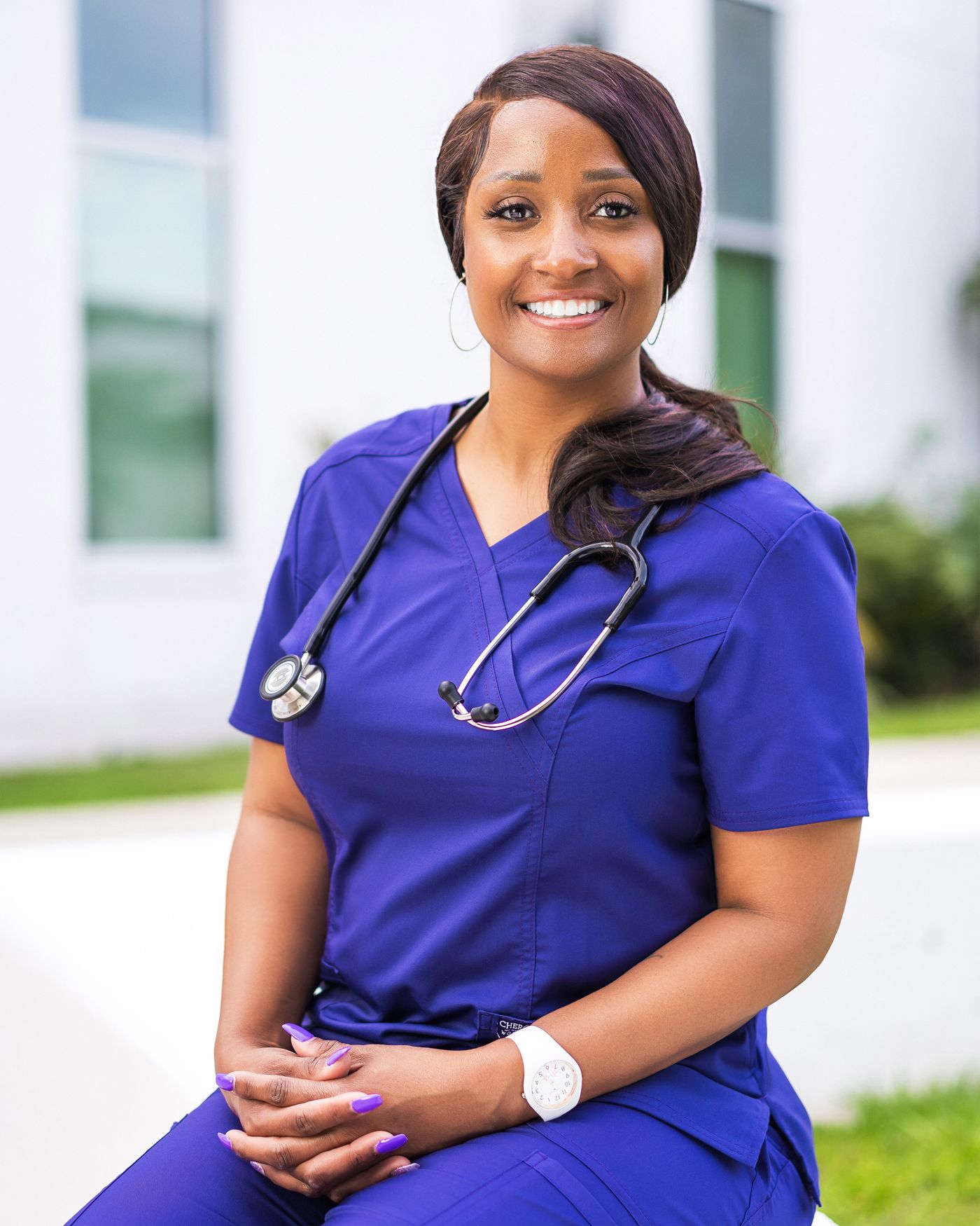 Mid-career nurse in scrubs with stethoscope outside a medical building